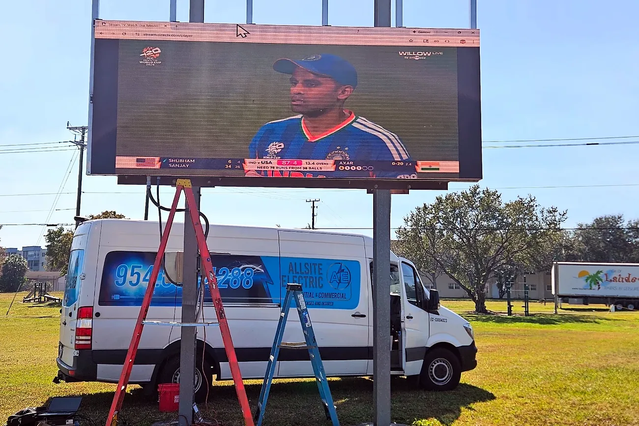Allsite Electric van and ladders under an outdoor sports park video board