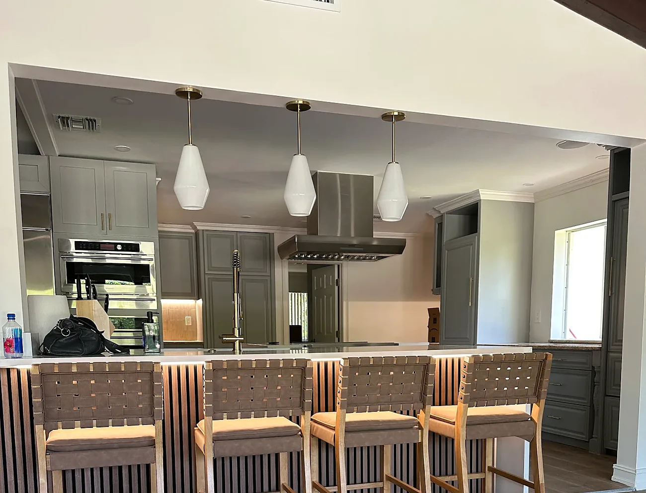 Three glass pendant lights over a kitchen island with bar stools and recessed lights