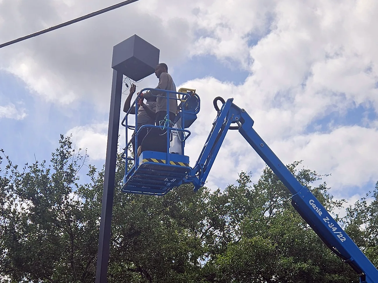 Electrician in a boom lift repairing a parking lot pole light