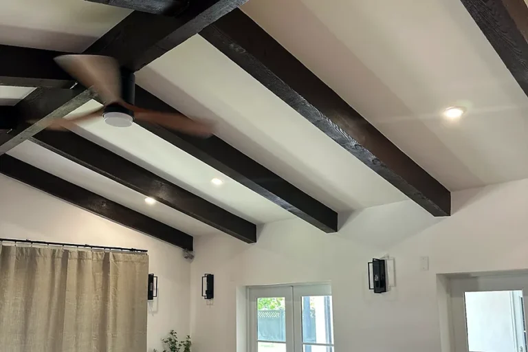 Ceiling fan and wall sconces installed in a living room with a vaulted beamed ceiling